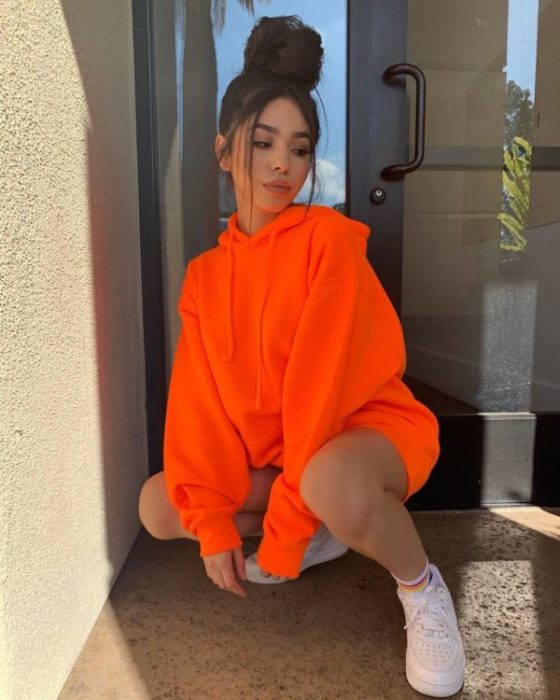 Chica agachada con una sudadera oversize color naranja nenón