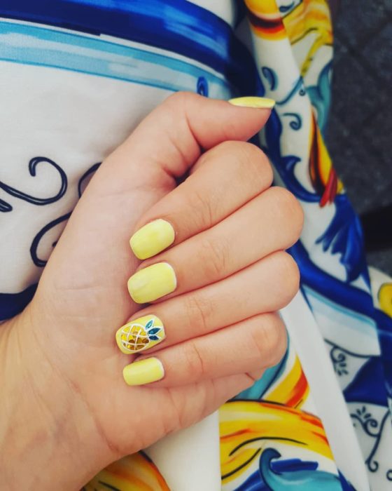 Manicura de uñas en tono amarillo con decorado de una piña en un costado