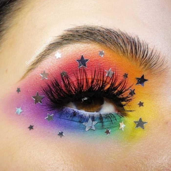 Maquillaje de arcoíris en colores azul, morado, amarillo, naranja, rosa con decorado de estrellas plateadas