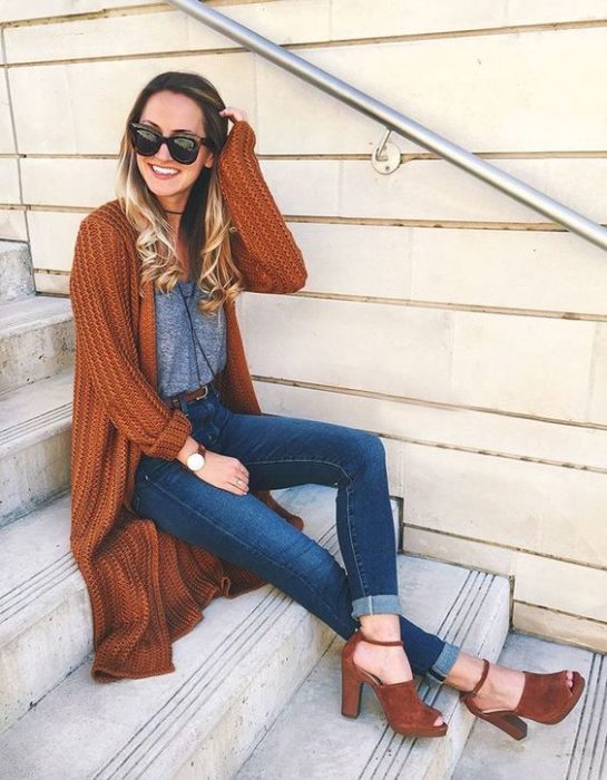 Chica sentada en escaleras con jeans, blusa gris y cardigan naranja