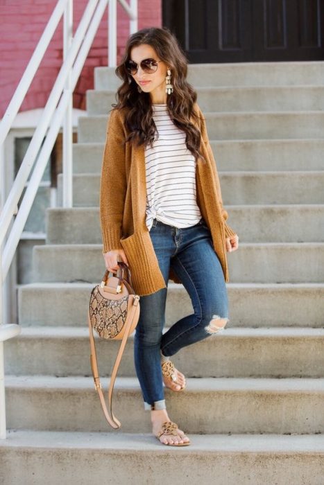 Mujer con jeans rotos en la rodilla, con blusa de rayas y cardigan amarillo mostaza