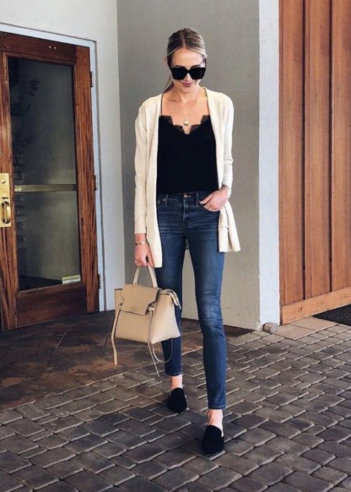 Chica delgada con jeans oscuros, blusa negra y cardigan blanco