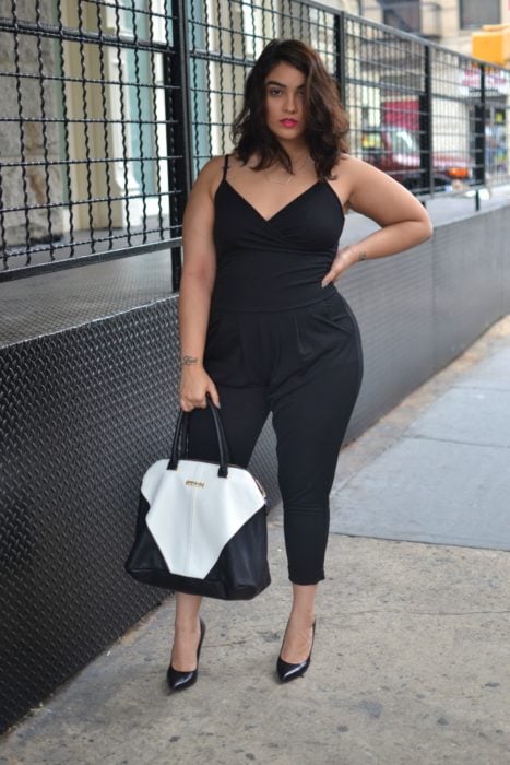 Chica curvy usando un jumpsuit de color negro con zapatillas negras y un bolso de color blanco 