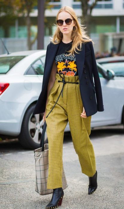 Chica rubia caminando por la calle con saco negro y paper bag pants amarillos