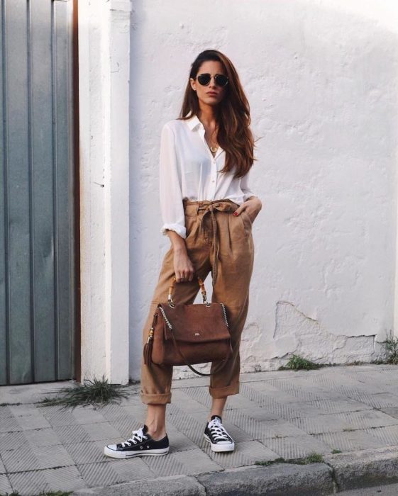 Mujer delgada de cabello largo con blusa blanca y paper bag pants cafés con converse negros