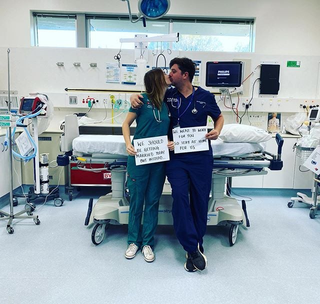 Pareja de doctores sosteniendo un cartel y besándose mientras están en un quirofano 
