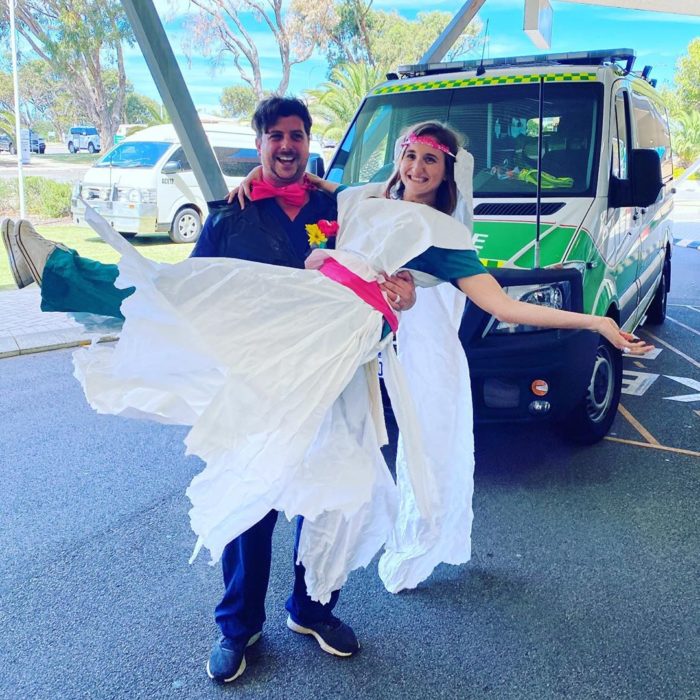 Chico sosteniendo a una chica en brazos mientras está usando un vestido de novia hecho con papel y bolsas de basura 