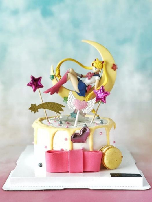 Pastel de Sailor Moon con base de fondant blnaca, una figurilla de Serena en sobre una luna y demás detalles