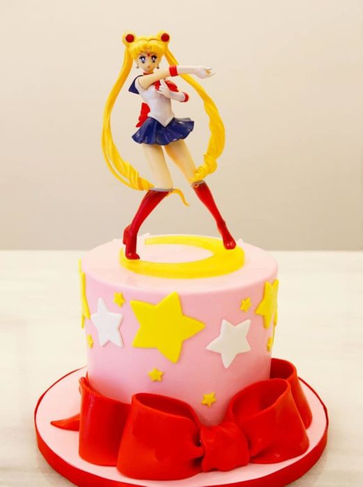 Pastel de Sailor Moon con una figurilla de juguete de Serena y fondant rosa