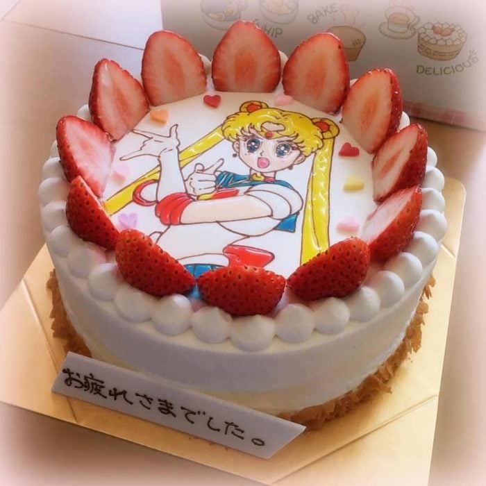 Pastel de Sailor Moon con Serena en el fondo, y decorado con fresas cortadas por la mitad al rededor