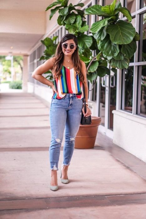 Chica morena con blusa de colores, jeans y tacones claros