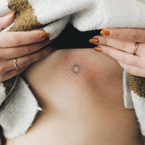 Tatuaje pequeño de un sol debajo del pecho de una mujer