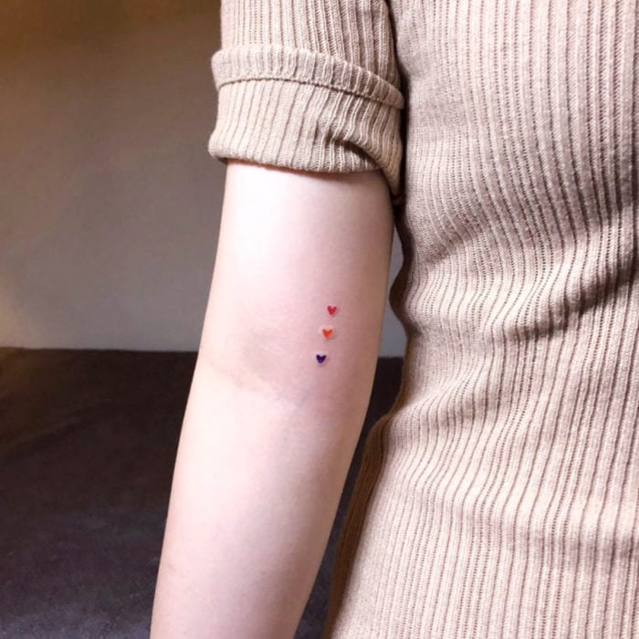 Tatuajes pequeños; minitatuaje de corazones rojo, anaranjado y morado en el brazo