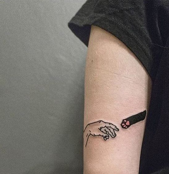 Tatuaje en el brazo de mano y patita de gato negro uniéndose