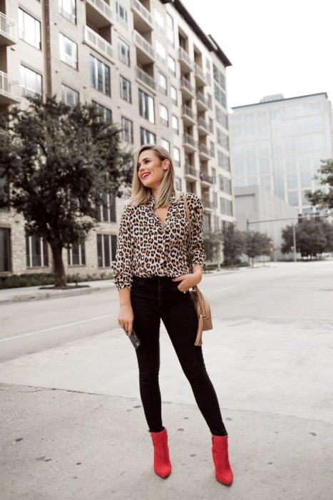 Chica rubia posa con pantalón negro, bluda de animal print y botines rojos