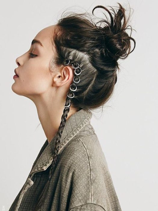 Chica posando de perfil con los ojos cerrados peinada con bun alto y una trenza lateral con argollas