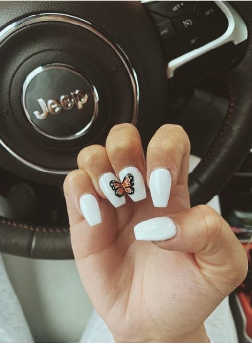 Manicura en tonos blancos con el diseño de una mariposa monarca