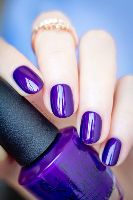 manos de mujer con manicura en tono morado uva con brillo