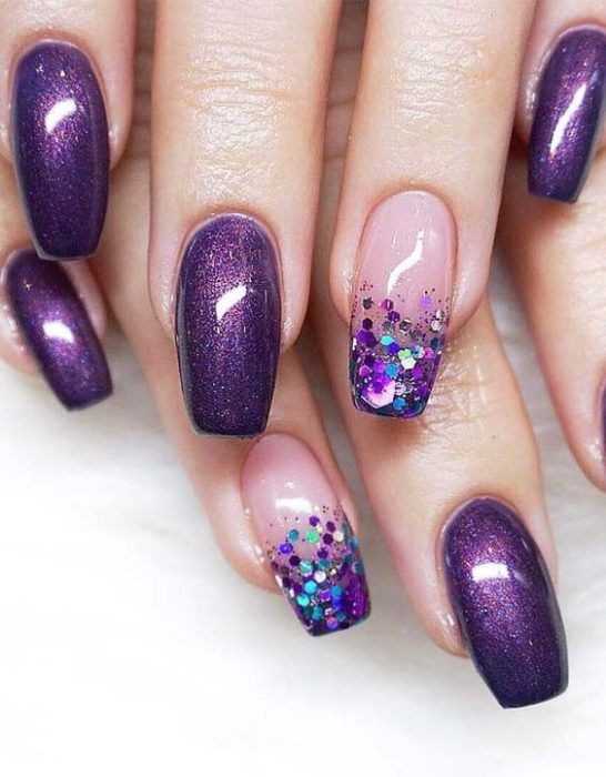 manos de mujer con manicura en tonos morados con efecto glitter y puntas con destellos