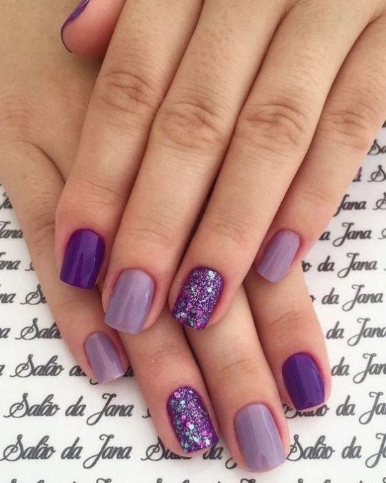 manos de mujer con manicura en tonos violeta, morado y purpura con destellos de glitter