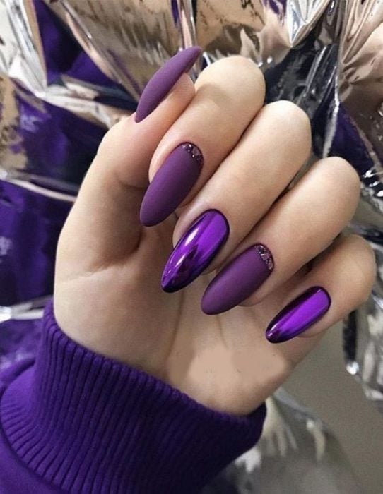 manos de mujer con manicura en tonos purpura con efecto metalizado y en estilo almendra