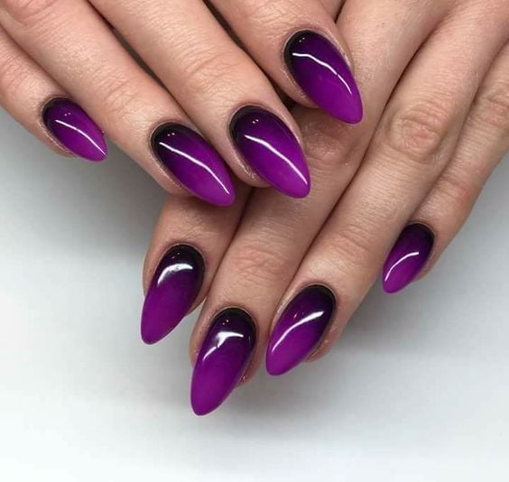 manos de mujer con manicura en tonos purpura con efecto degradado en estilo almendra