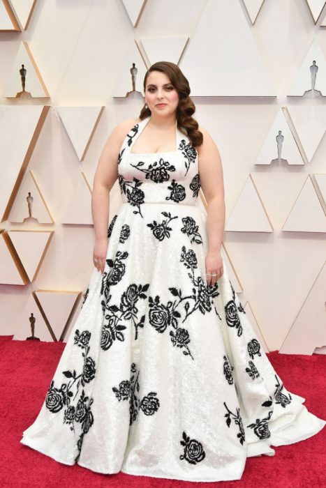 Beanie Feldstein usando un vestido largo de color blanco con un bordado de flores en color negro 