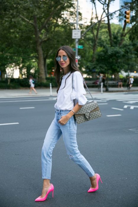 Chica cruzando la calle con pantalón de mezclilla, blusa blanca y stilettos rosas