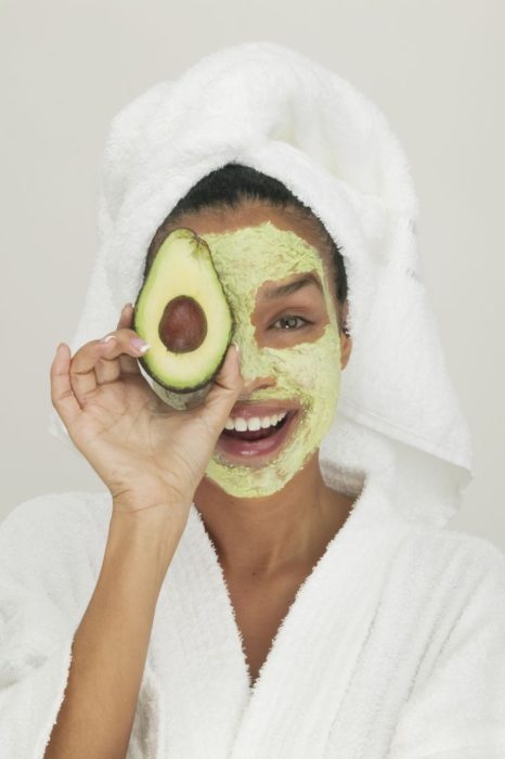 chica llevando mascarilla de aguacate dobre el rostro y una toalla enredada en la cabeza 