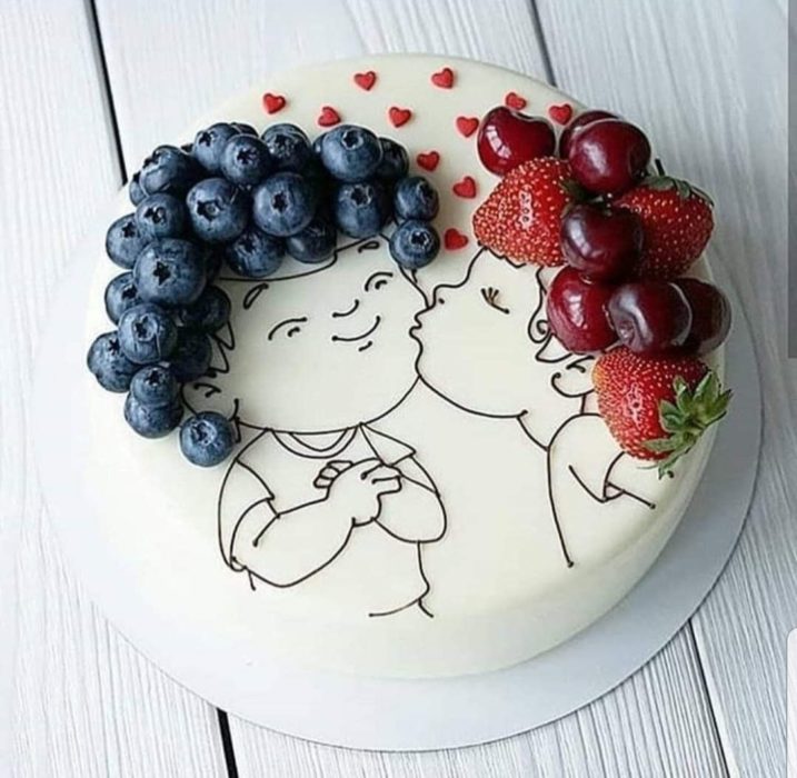 Pastel con betún blanco decordo con la silueta de niños con cabello rizado formado con fresas y uvas