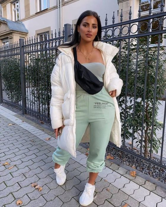 chica morena de cabello oscuro largo usando una chamarra blanca, pants deportivos color menta, tenis blancos y una cangurera negra de piel