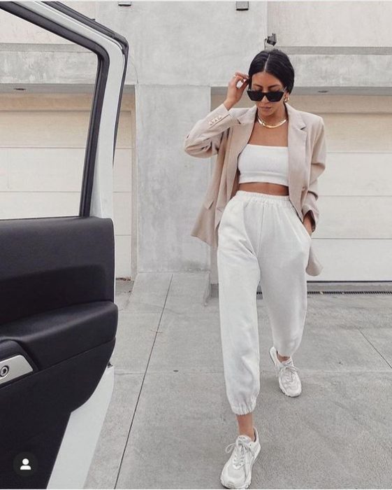 chica usando lentes de sol, top blanco, blazer beige, pantalones pants blancos y tenis deportivos blancos