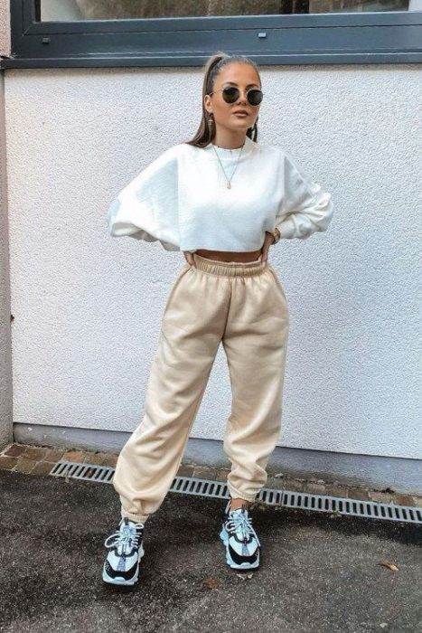 chica de cabello castaño con sudadera blanca, pants beige y tenis deportivos blanco y negro