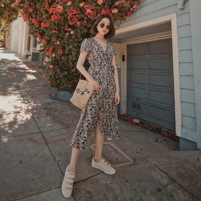 chica con cabello oscuro corto y vestido largo estampado, bolsa tejida beige y zapatos deportivos, lentes de sol