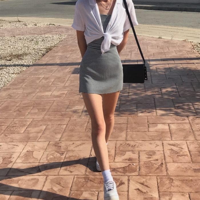 chica con vestido de cuadros blancos y negros, bolsa negra de piel, camisa blanca de manga corta y tenis deportivos blancos