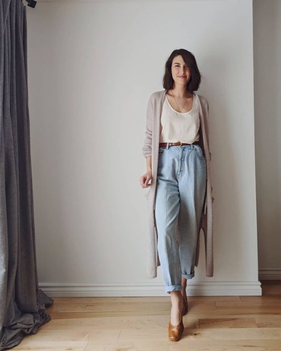 chica de cabello castaño usando un top blanco, cárdigan beige oversized, jeans slouchy y flats