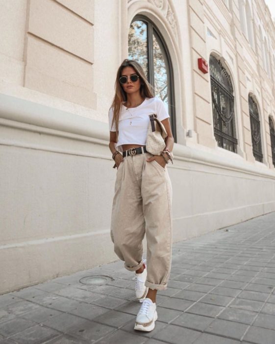 chica rubia con playera blanca de manga corta, cinturon negro, slouchy jeans de pana, lentes de sol y tenis blancos