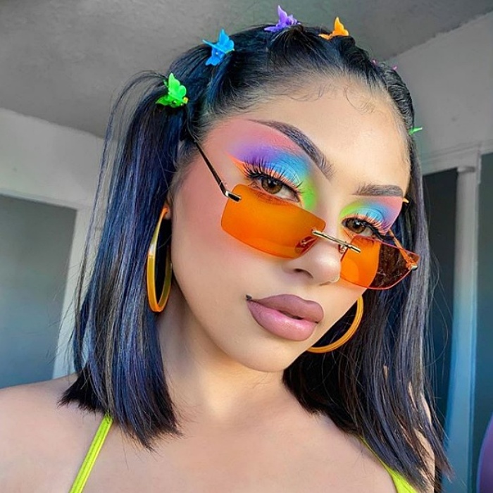 chica de cabello morado y azul usando maquillaje de arcoiris y lentes de sol anaranjados