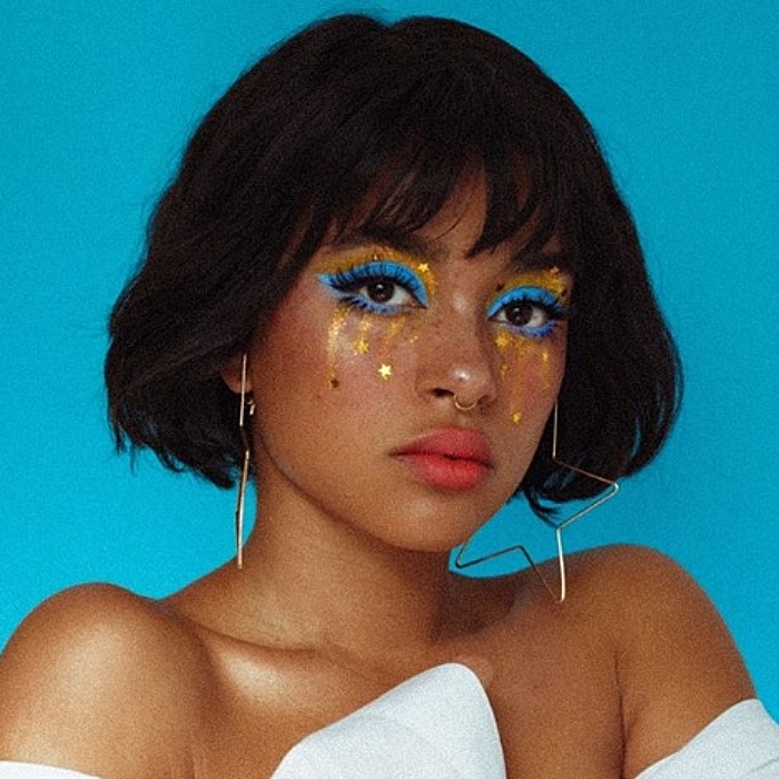 chica morena con cabello corto usando maquillaje de sombras azules, glitter dorado y stickers de estrella