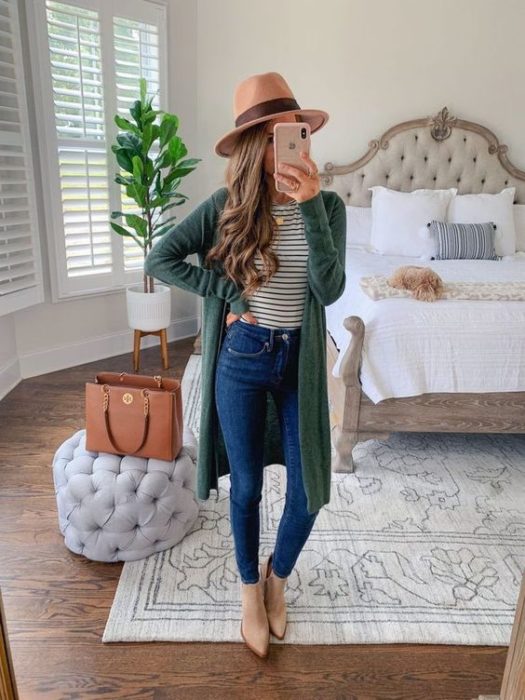 Mujer se toma selfie frente al espejo con cardigan verde y sombrero beige