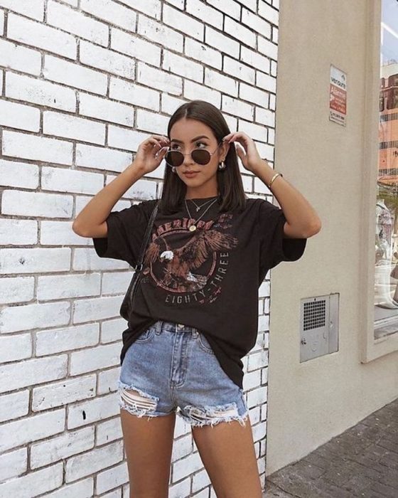 chica de cabello castaño con lentes de sol, camiseta negra, shorts de mezclilla