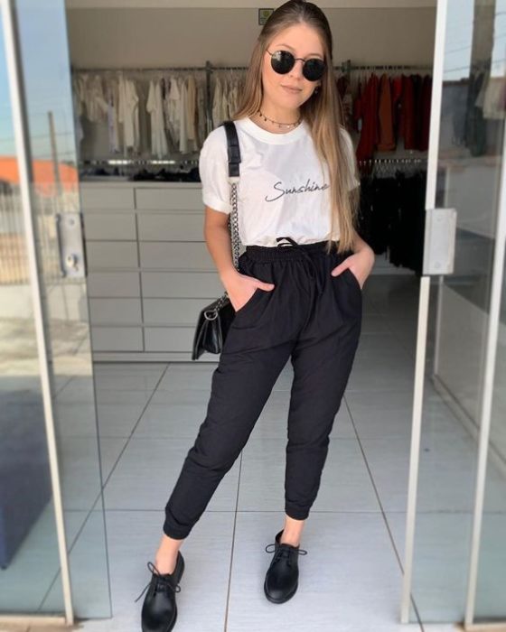 Chica usando jogger negro, zapatos negros y playera blanca