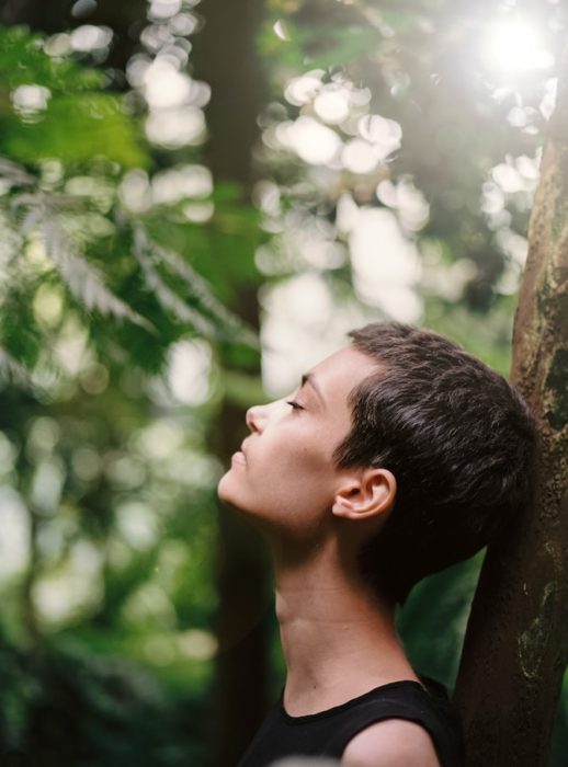 Mujer recargada en un árbol respirando profundo