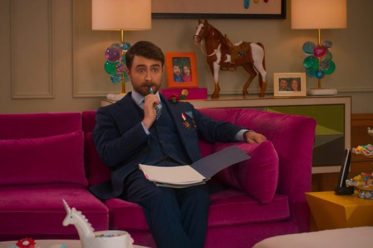 Daniel Radcliffe en la película Unbreakable Kimmy Schmidt: Kimmy contra el reverendo, sentado en un sofá rosa