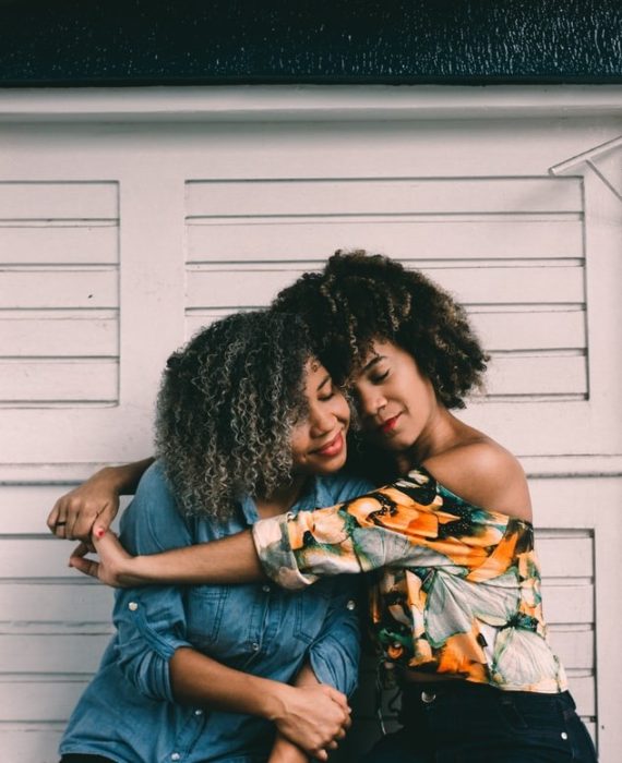 Chicas de cabello rizado estilo afro abrazadas y sonriendo 