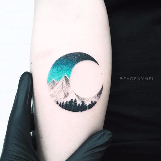 Tatuaje de una media luna con u paisaje interior de las montañas