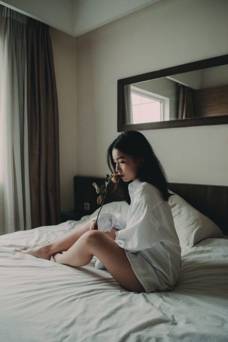 Chica sentada en la cama oliéndo una flor