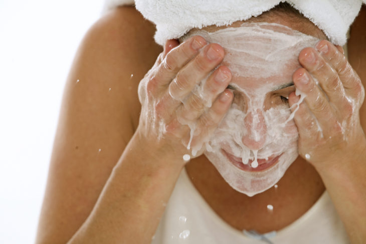 Chica enjuagandose su cara después de haber aplicado una mascarilla