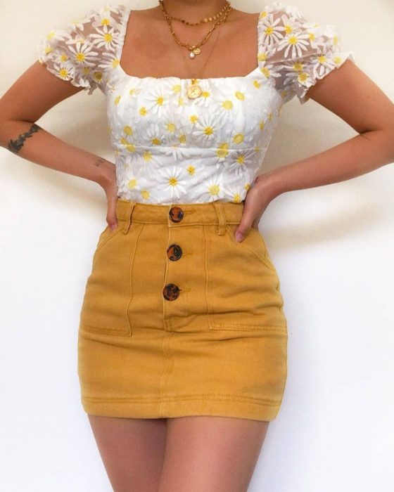 Chica usando mini falda color mostaza y blusa blana con detalles de girasoles