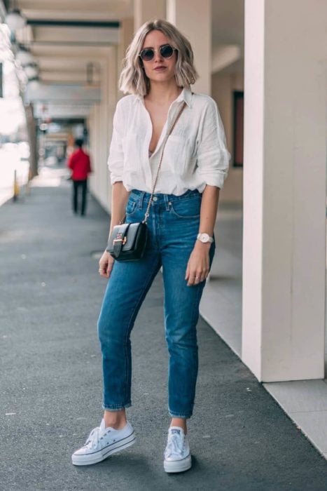 Chica usando una blusa blanca con escote, jeans y tenis 